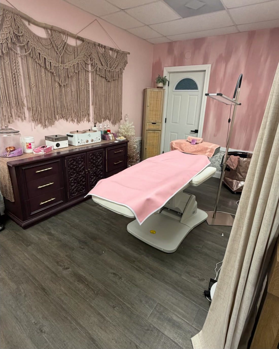 The waxing room: pink walls, a macrame hanging, and the table made up and waiting.