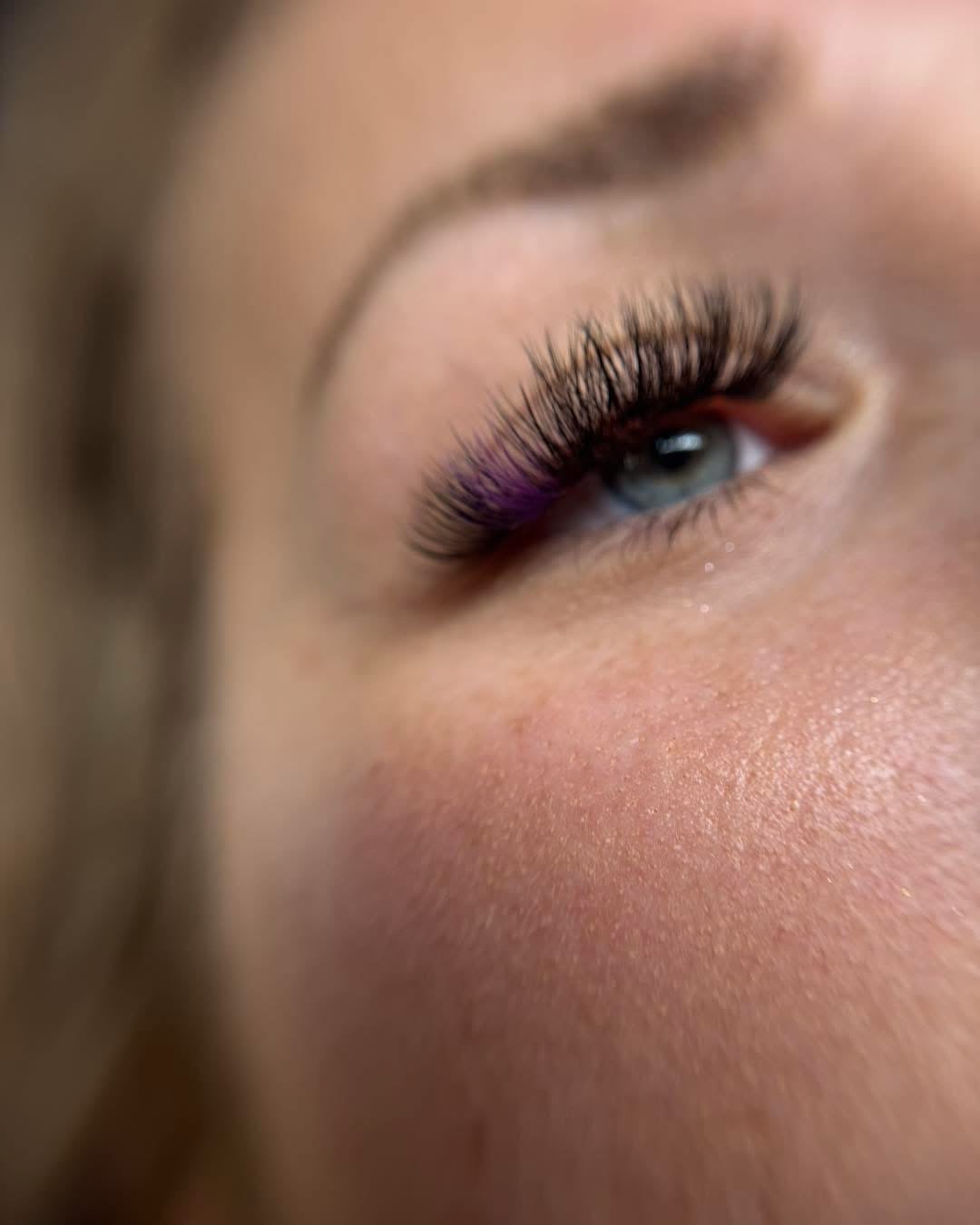 A close-up of lash extensions with soft violet tips at the outer corner.